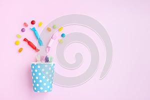 Different kinds of colorful candy out of a blue paper cup with white dot on pink background