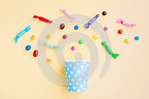 Different kinds of colorful candy out of a blue paper cup with white dot on yellow background