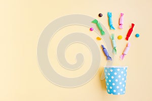 Different kinds of colorful candy out of a blue paper cup with white dot on yellow background