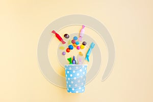 Different kinds of colorful candy out of a blue paper cup with white dot on yellow background