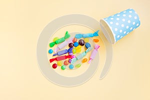 Different kinds of colorful candy out of a blue paper cup with white dot on yellow background