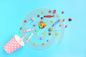 Different kinds of colorful lollipop and candy out of a pink paper cup with white dot on blue background