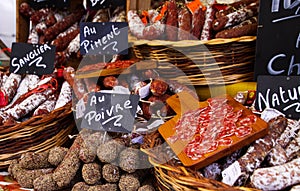 Different kinds of French salami provencale presented in wicker baskets with handwritten chalk boards on farmer market