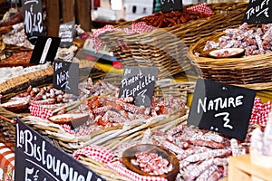 Different kinds of French salami provencale presented in wicker baskets with handwritten chalk boards on farmer market