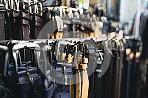 Different kinds of leather colored belts for jeans and suits hanging by the buckle in clothes store display