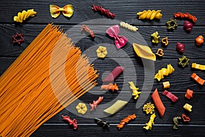 Different kinds of pasta on black background. Yellow conchiglie, color farfalline, orange tomato spaghetti, ping, green and