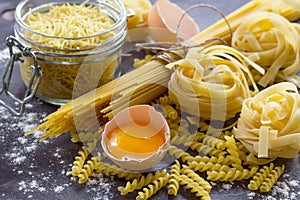Different kinds of pasta spaghetti, fusilli, fettuccine and raw egg yolk on the kitchen wooden table