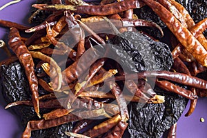 Different kinds of sun-dried hot peppers stacked haphazardly on a purple-colored background. photo