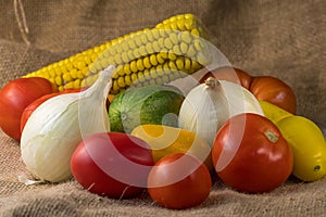 Different kinds of vegetables lie together on one table, tomatoes, onions and corn