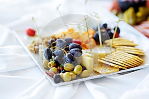 Different kinds of wine snacks: cheeses, crackers, fruits and olives on white table