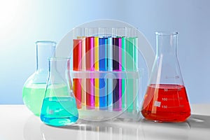 Different laboratory glassware with colorful liquids on white table against grey background