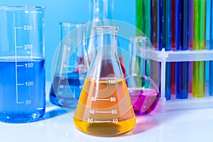 Different laboratory glassware with colorful liquids on white table against light blue background