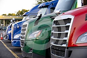 Different make big rig semi trucks tractors stands in row on truck stop parking lot marked with lines