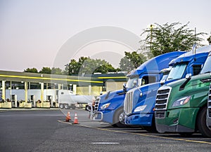 Big rig semi trucks standing in row on the truck stop with fuel station at twilight