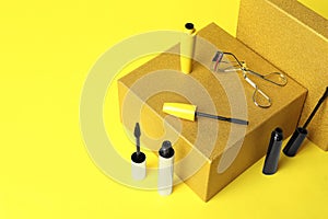 Different mascaras and eyelash curler on yellow background. Makeup product