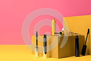 Different mascaras and eyelash curler on yellow, space for text. Makeup product