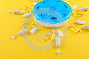 Different medicines for one week and a pills box on yellow background