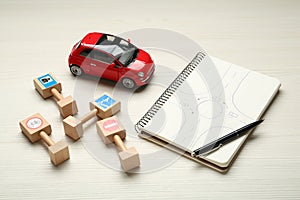 Different miniature road signs, car and notebook with sketch of roundabout on white wooden background. Driving school