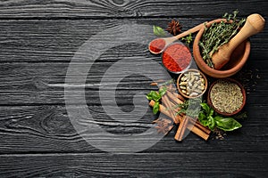 Different natural spices and herbs on black wooden table, flat lay. Space for text