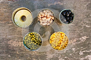 Different open canned food on old wooden background.