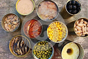 Different open canned food on old wooden background.