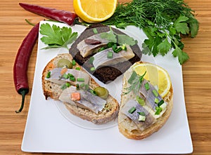 Different open sandwiches with pickled herring on square dish