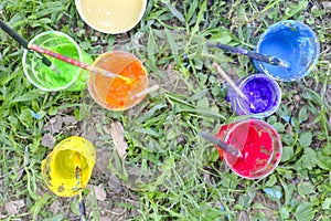 Different painting colours with brushes on a palette on a grass ground