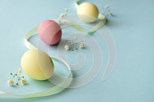 Different pastel color Easter eggs laid and arranged in beautiful composition with white wildflowers. Greeting card with copy text