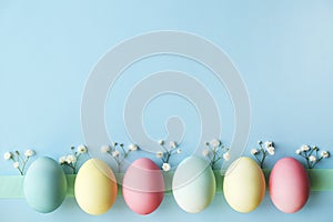 Different pastel color Easter eggs laid and arranged in beautiful composition with white wildflowers. Greeting card with copy text