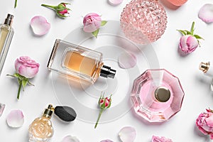 Different perfume bottles and flowers on white, top view photo