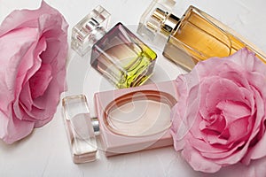 Different perfume bottles with pink roses on the white background. Perfumes, cosmetics, a collection of fragrances.