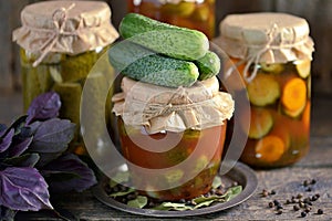 Different pickled cucumbers - whole and slices with onions, carrots in tomato juice on an old wooden background.