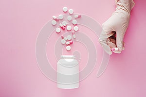 Different pills drugs or tablets spilling out of a white plastic medicine bottle. Female doctor hand with capsule. Health care