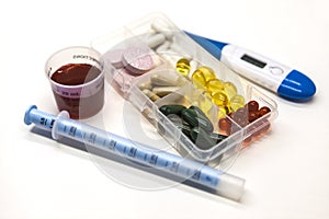 Different pills, medications in the box for drugs with medicine with a syringe and with thermometer on white background closeup.