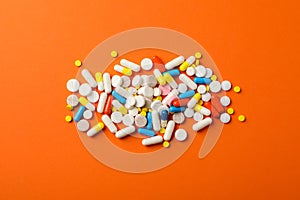 Different pills on orange background, top view