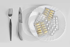 Different pills on a plate with cutlery. Means for suppressing appetite