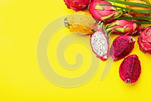 Different pitahaya fruits and palm leaf on yellow background, flat lay. Space for text