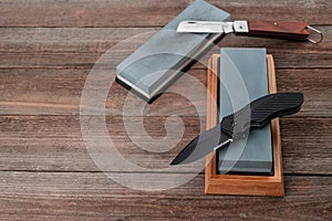 Different pocket knives and whetstones on rustic wooden background