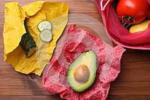 Different products in beeswax food wraps on wooden table, flat lay