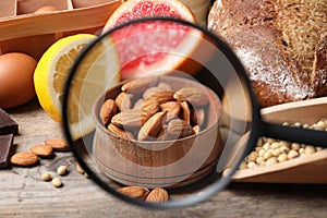 Different products with magnifier on almonds, closeup. Food allergy concept