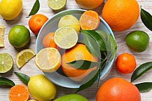 Different ripe citrus fruits with green leaves on white wooden table, flat lay