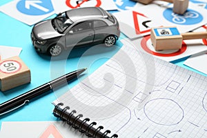Different road signs, notebook with sketch of roundabout and toy car on light blue background. Driving school