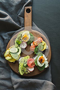 Different sandwiches with vegetables, eggs, avocado, tomato, rye bread on black chalkboard background. Top vew. Appetizer for part