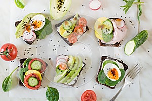 Different sandwiches with vegetables, eggs, avocado, tomato, rye bread on light marble table. Top view. Appetizer for party. Flat