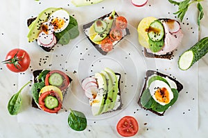 Different sandwiches with vegetables, eggs, avocado, tomato, rye bread on light marble table. Top vew. Appetizer for party. Flat l