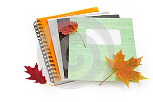 Different school exercise books with several autumn leaves