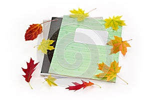 Different school exercise books with several autumn leaves