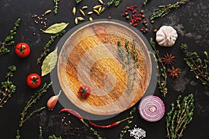 Different seasoning for cooking on a dark background. Empty wooden plate, spices, herbs, vegetables. Top view, flat lay