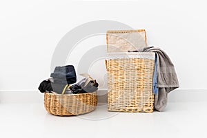 Different shape of wicker basket full of laundry clothes in clean white wall background inside bedroom.