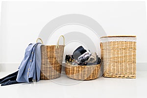 Different shape of wicker basket full of laundry clothes in clean white wall background inside bedroom.